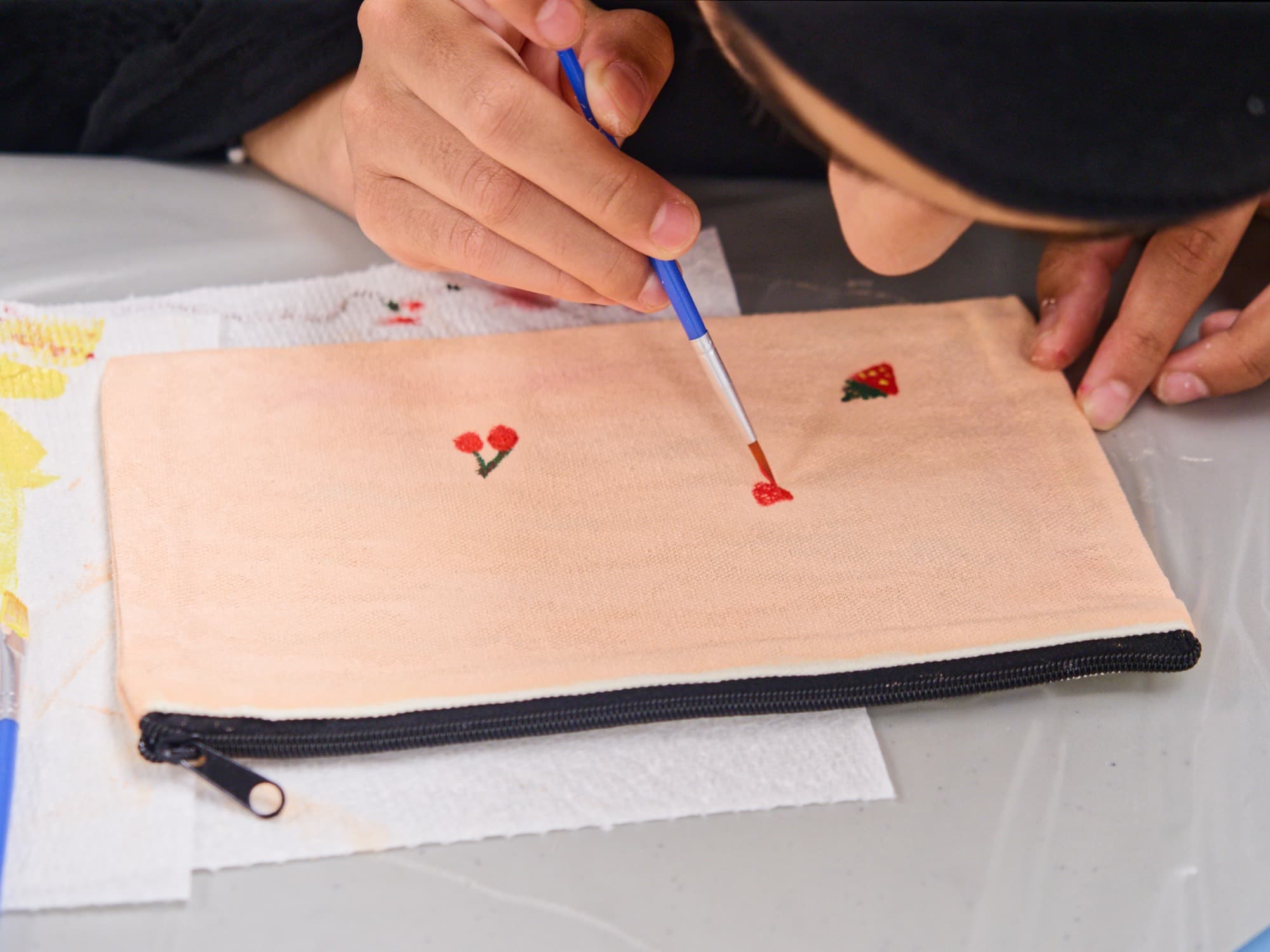 Close-up of someone painting small flowers onto a fabric pouch