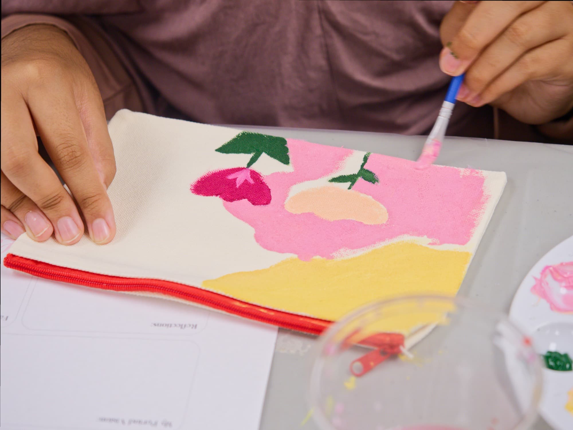 A pouch being hand-painted with pink and yellow flowers
